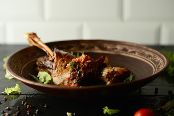 Roasted goose leg, sauce, herbs and tomatoes in a clay bowl on wooden background