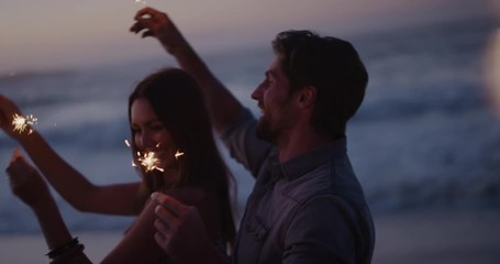 happy young couple waving sparklers dancing celebrating new years eve on calm beach sunset background sparkle firework - Powered by Adobe