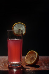 Clear glass with red drink with lemon slice on dark background