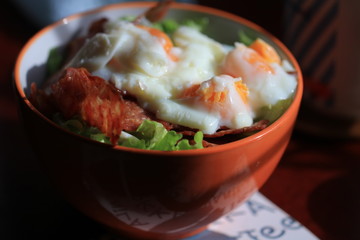Close up boiled eggs and bacon on rice in orange bowl