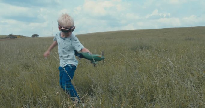 Cute little dreamer kid boy wearing pilot glasses playing with toy airplane in the field, DX. 4K UHD 60 FPS SLO MO 