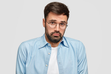 Confused insulted bearded man looks with miserable doubt expression, has to make serious decision...