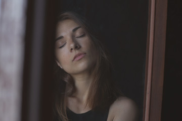 Fototapeta premium Sensual authentic portrait of young serious lady posing through dirty window, communicating with camera. Real life and art concept. Human feelings, emotions and expressions in natural conditions.