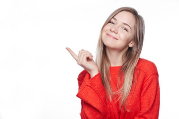 Satisfied glad young blond woman with charming smile points at upper left corner, shows blank space for promotional content, advertises something, wears stylish red loose sweater, isolated on white.