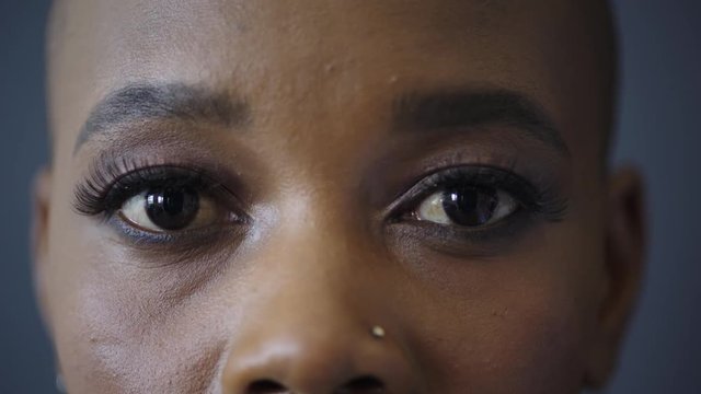 close up of beautiful black woman eyes opening looking at camera wearing makeup nose piercing