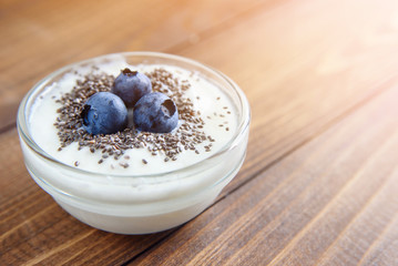 Yogurt in a glass transparent jar with chia seeds and blueberries on a wooden background.