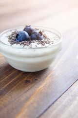 Yogurt in a glass transparent jar with chia seeds and blueberries on a wooden background.