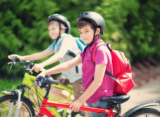 Children with rucksacks riding on bikes in the park near school. Pupils with backpacks outdoors