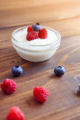 Yogurt in a glass transparent jar with fresh blueberries and raspberries on a wooden background.