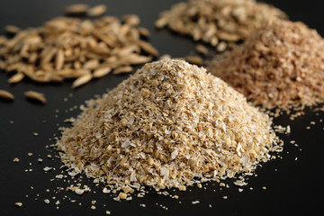 Bran oatmeal with a large grind, with grains of oats and wheat on a black background. Useful,...