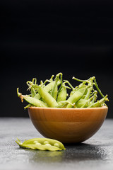 Photo of green pea pods in wooden plate on black table with pod