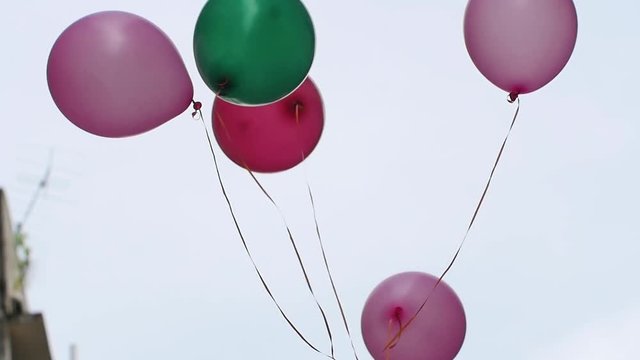 An arrangement of colorful helium filled balloons drifts slowly up into the sky in slow motion.