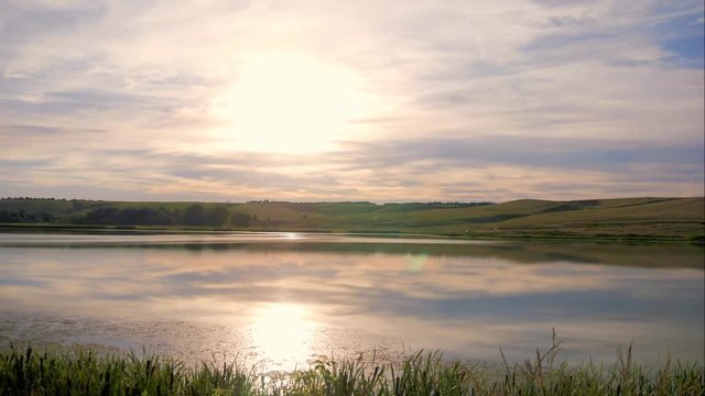 Time lapse of clouds dancing in the wind above a beautiful pond. Sunset footage with moving clouds reflection in a pond.