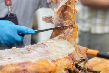 Cutting the mutton hulk fried on a grill for the Uzbek pilaf. Male hands keep a povarsky knife in gloves and cut meat