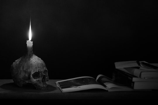 Skull with candle on head which has candlelight lighting for read and learn on the wooden plank in dark room