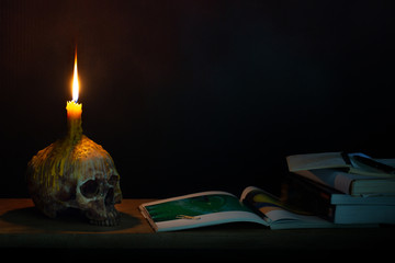 Skull with candle on head which has candlelight lighting for read and learn on the wooden plank in...