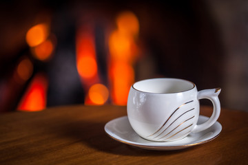 White cup of tea or coffee near fireplace on wooden table. Winter and Christmas holiday concept
