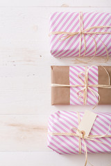 Top view on Christmas, birthday or any other celebration gift wrapped in pink striped paper and decorated with ribbon and tag on white wooden background