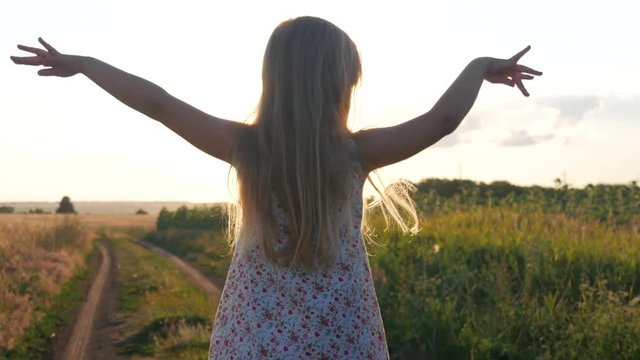 Little girl to wave hands on meadow with sunset. Happy pretty girl in field at sunset.