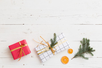 Top view on nice Christmas presents decorated with ribbons, tree branch and orange slices on white wooden background. Gifts. Holiday season.