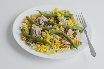 Colorful fusilli pasta with tuna, green beans and yellow sweet corn served on white table with fork. Healthy and balanced eating concept