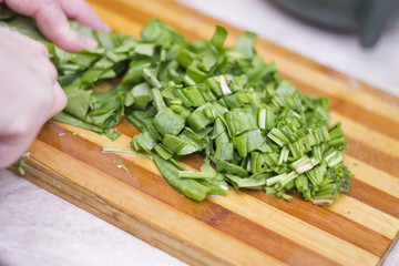 Woman cutting sorrel by knife on the wooden cooking desk