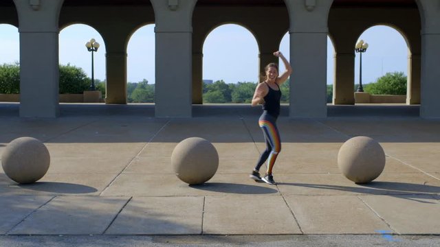 Fit millennial girl dances and gets her groove on in front of arches in the park.