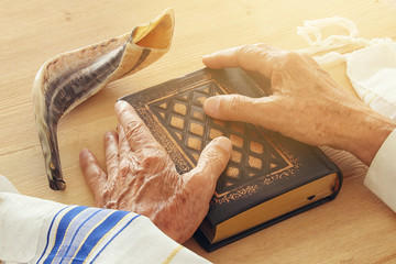 Old Jewish man hands holding a Prayer book, praying, next to tallit and shofar (horn). Jewish...