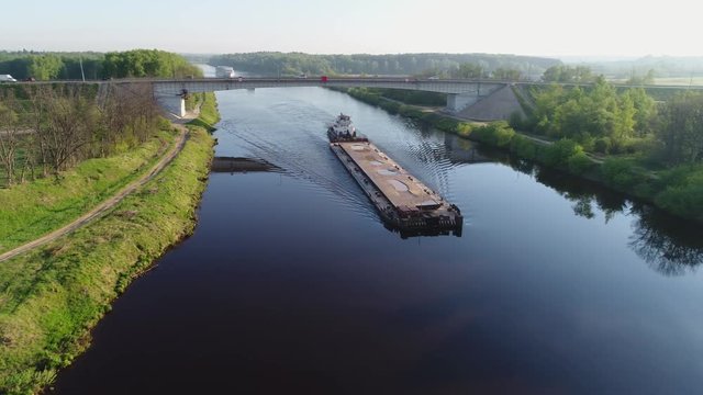 Aerial view. The tug and the barge loaded with river sand swims under the concrete road bridge on which the car ride. The cargo ship sails on the Moscow Channel on a sunny summer day.