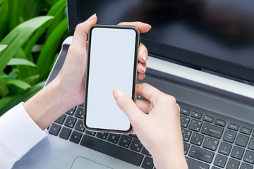 Mockup Of Business Woman Holding Mobile Phone with blank screen and laptop background.