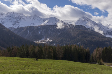 View over snowy alps with a green meadow in foreground and sky with some clouds in background