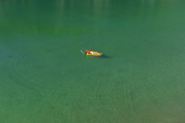 A young woman spends leisure time on an inflatable  sun bed in the middle of a green lake. She wears a white swim suit and enjoys the summer sun as she relaxes on the sun bed. 