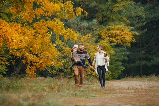 Young parents with their daughter walk at forest path with dog in autumn forest.