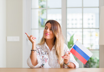 Young woman at home holding flag of Russia very happy pointing with hand and finger to the side