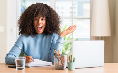 African american woman studying at home using a computer laptop very happy and excited, winner expression celebrating victory screaming with big smile and raised hands