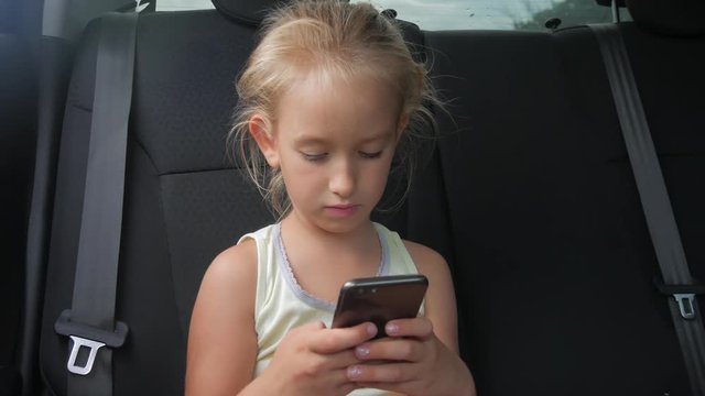 Young attractive blonde girl sitting in the car and use smartphone.
