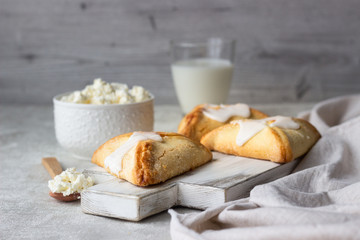 Pasties or buns with cottage cheese and powdered sugar glaze on a light background. Traditional Russian bun Sochnik. Selective focus. 