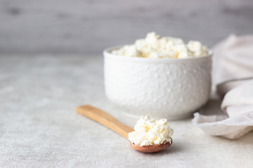 Fresh farming cottage cheese in a white ceramic bowl with a spoon on a light background. Dairy products. Selective focus. Copy space