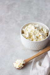 Fresh farming cottage cheese in a white ceramic bowl with a spoon on a light background. Dairy products. Selective focus. Copy space