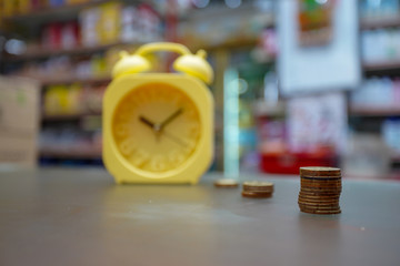 Yellow alarm clock and fingers of business man putting on coin and looking for saving money, collect money with earning bank deposit interest and take time. Business ideas concept. Selective focus.