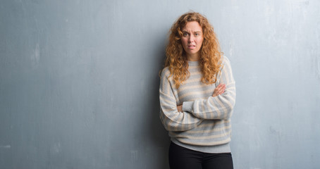 Young redhead woman over grey grunge wall skeptic and nervous, disapproving expression on face with crossed arms. Negative person.