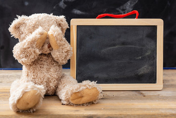 Teddy bear covering eyes and a blank blackboard, space for text