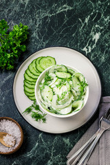 Obraz premium Creamy cucumber dill salad with yogurt dressing on dark marble background. Top view, space for text.
