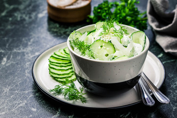 Creamy cucumber dill salad with yogurt dressing on dark marble background. Selective focus, space...