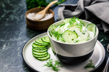 Creamy cucumber dill salad with yogurt dressing on dark marble background. Selective focus, space...
