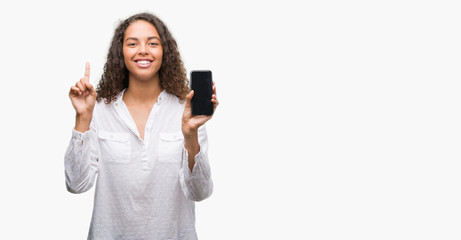 Fototapeta premium Young hispanic woman using smartphone surprised with an idea or question pointing finger with happy face, number one