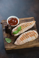 Barbecued turkey breast fillet served on a rustic wooden chopping board, vertical shot
