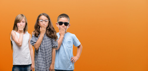 Group of boy and girls kids over orange background cover mouth with hand shocked with shame for...