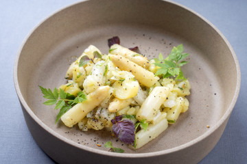 Modern style traditional German potato salad with white asparagus and gherkin as close up on a plate