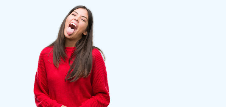 Young beautiful hispanic wearing red sweater sticking tongue out happy with funny expression. Emotion concept.